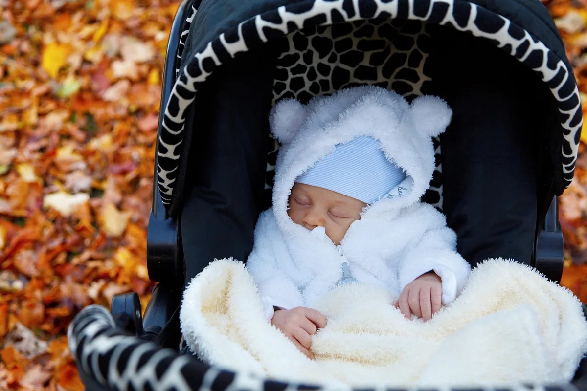 Poussette avec pare-soleil et porte-bébé posés près d'une porte-fenêtre ensoleillée