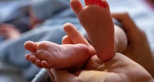 Parent habille un bébé en couches légères près d'une table à langer, lumière naturelle