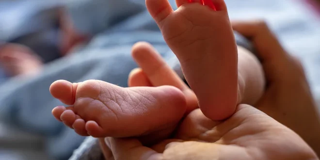 Parent habille un bébé en couches légères près d'une table à langer, lumière naturelle
