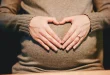 Mains anonymes posées sur un ventre de femme enceinte, intérieur lumineux
