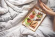 Chambre en journée avec un lit, coussin de grossesse et une valise prête pour la maternité