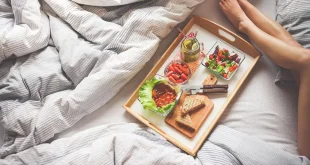 Chambre en journée avec un lit, coussin de grossesse et une valise prête pour la maternité