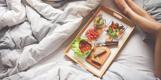 Chambre en journée avec un lit, coussin de grossesse et une valise prête pour la maternité